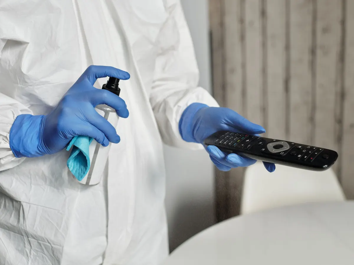 Gloved hand spraying disinfectant on a remote control